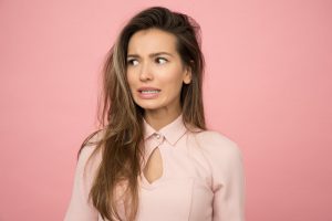 A woman wearing a pink top has a look of uncertainty on her face. Music therapy can help her with managing uncertainty.