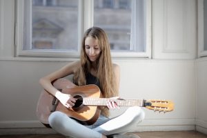 A teen girl plays a brown acoustic guitar. She might benefit from child and teen counseling with SoundWell Music Therapy