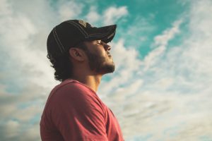 man wearing black cap with eyes closed under cloudy sky appears to be engaged in mindfulness meditation