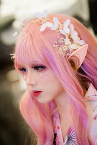 a female-appearing teen wearing elf ear and floral headdress is engaging in adolescent identity development through cosplay