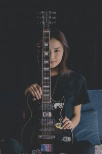 a teen sits with guitar in front of her and she is wanting to engage in identity expression through music